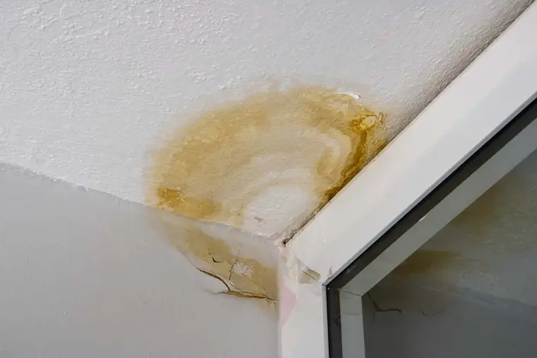 Brown water stain spreading across a top-floor ceiling corner after a roof leak
